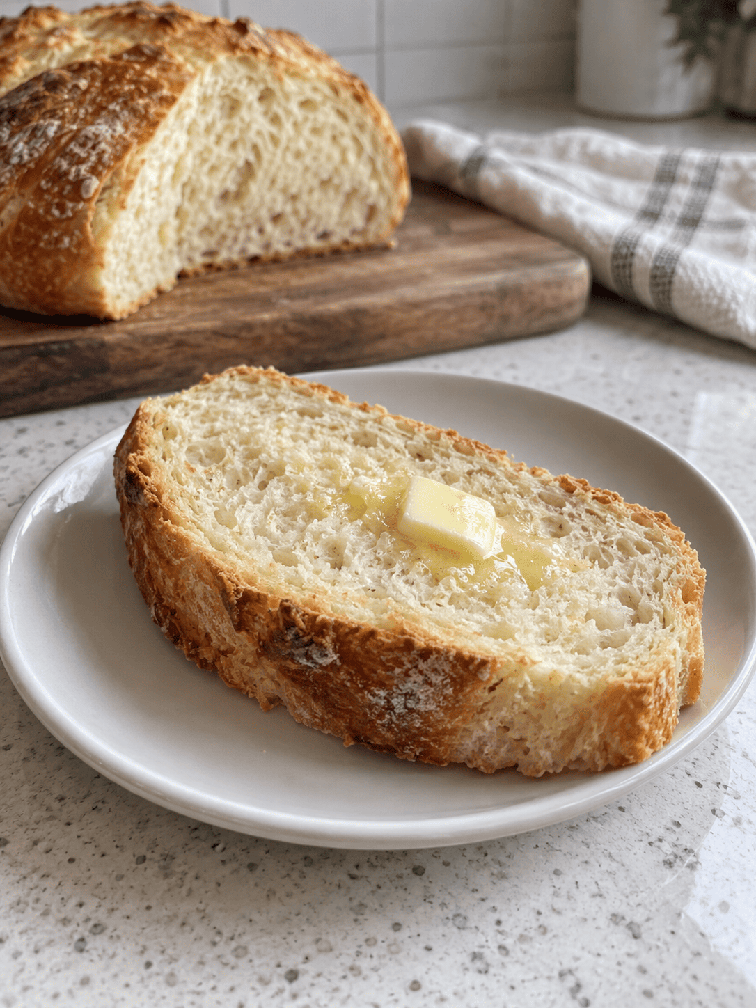 One serving of Crock Pot Bread with butter on a white ceramic plate