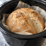 Crock Pot Bread with a golden rustic crust in a parchment-lined slow cooker